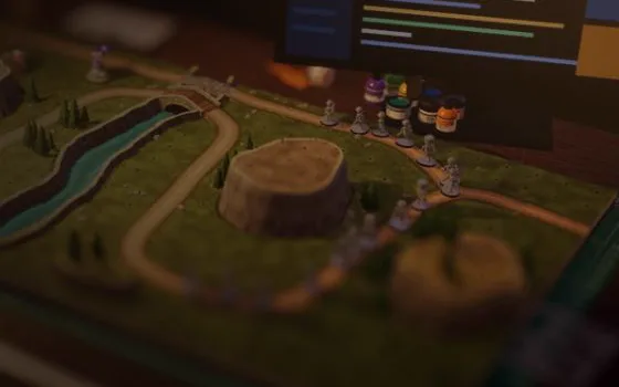 A painted tabletop board: a river, a winding path and a column of grey miniatures marching on it